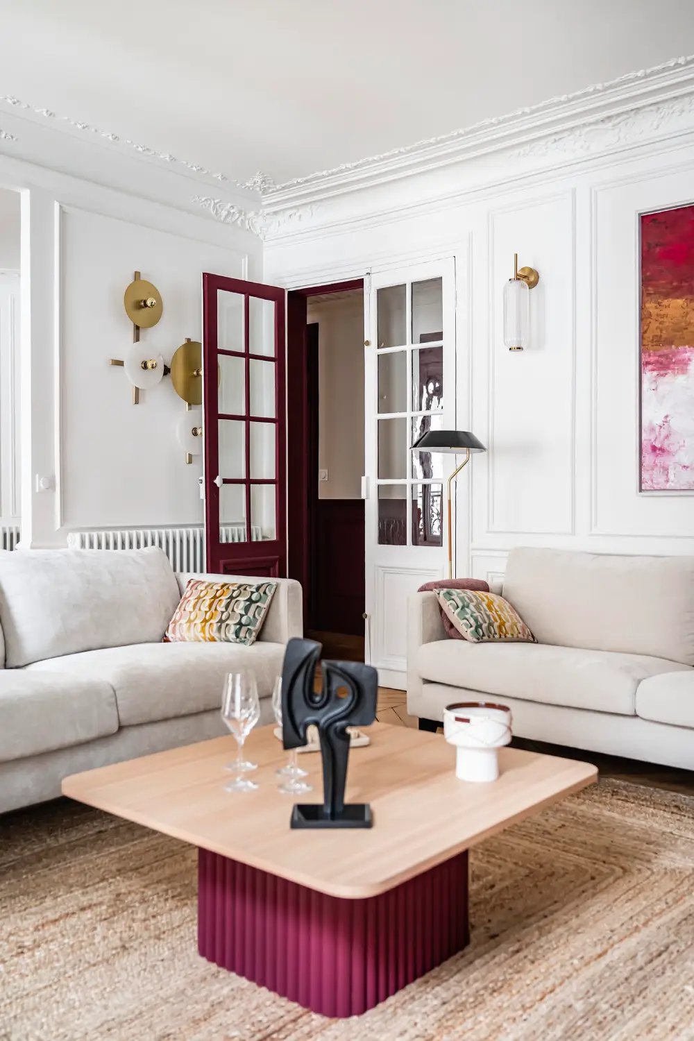 Grand salon haussmannien lumineux avec deux canapés blancs, table basse au piétement bourgogne et moulures
